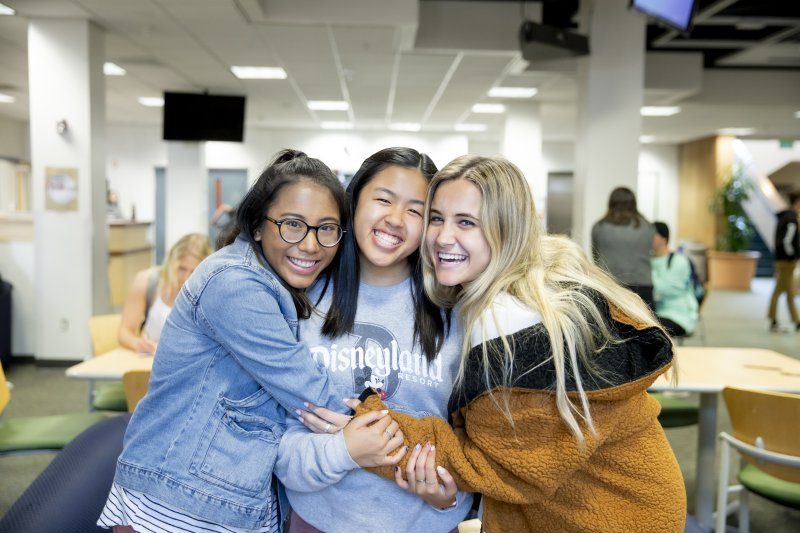 Three female students are hugging each other and are smiling.